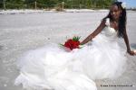 braut sitzt im weissen Hochzeitskleid im Sandstrand und rotem Rosen Bouquet