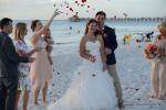 Hochzeitspaar und die Gaeste werfen Rote Rosenblaetter am Strand