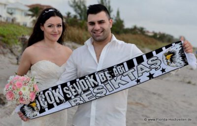 Braut und Braeutigam mit Banner und Brautstrauss am Strand von Delray Beach in Florida