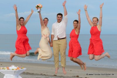 Springende Hochzeitsgesellschaft Ladies in wunderschoenen Orangefarbenen Kleidern am Strand von Delray Beach