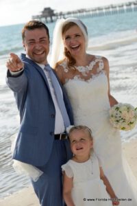 Hochzeitspaar am Strand von Naples mit Pier im Hintergrund zeigt auf Delfine