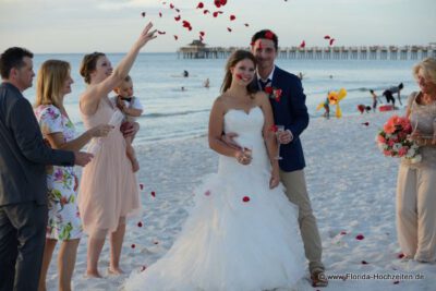 Hochzeitspaar und die Gaeste werfen Rote Rosenblaetter am Strand