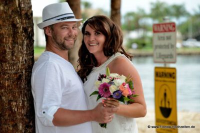 Lachendes Brautpaar mit Brautstrauss am Strand-001