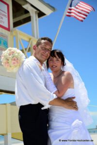 Hochzeitspaar mit USA Flagge vor Lifeguardhaeuschen in Miami Beach