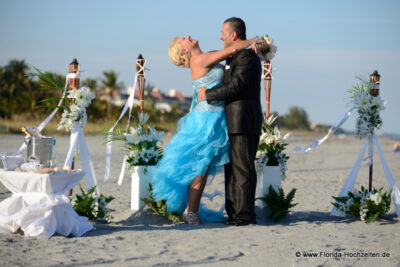 Glueckliches Hochzeitspaar Braut traegt Tuerkis und lehnt sich gluecklich zurueck in zauberhafter Dekoration am Strand von Florida