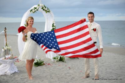 US Flagge mit Hochzeitspaar und Rosenbogen am Strand
