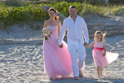 Happy Family Braut und Kind in Rosa Kleidern auf dem Weg zur Hochzeit am Strand