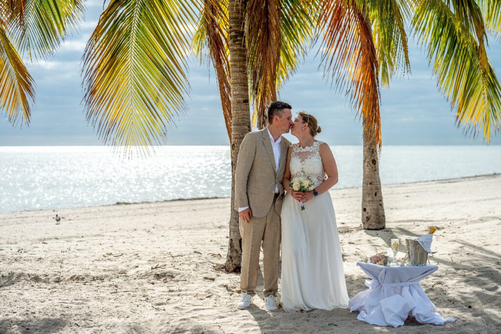 Hochzeitspaar am Strand von Key Biscayne unter Palmen küsst sich