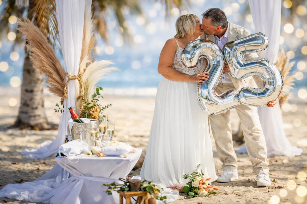 Brautpaar am Strand hält eine 25 in den Händen und küsst sich unter dem Arch