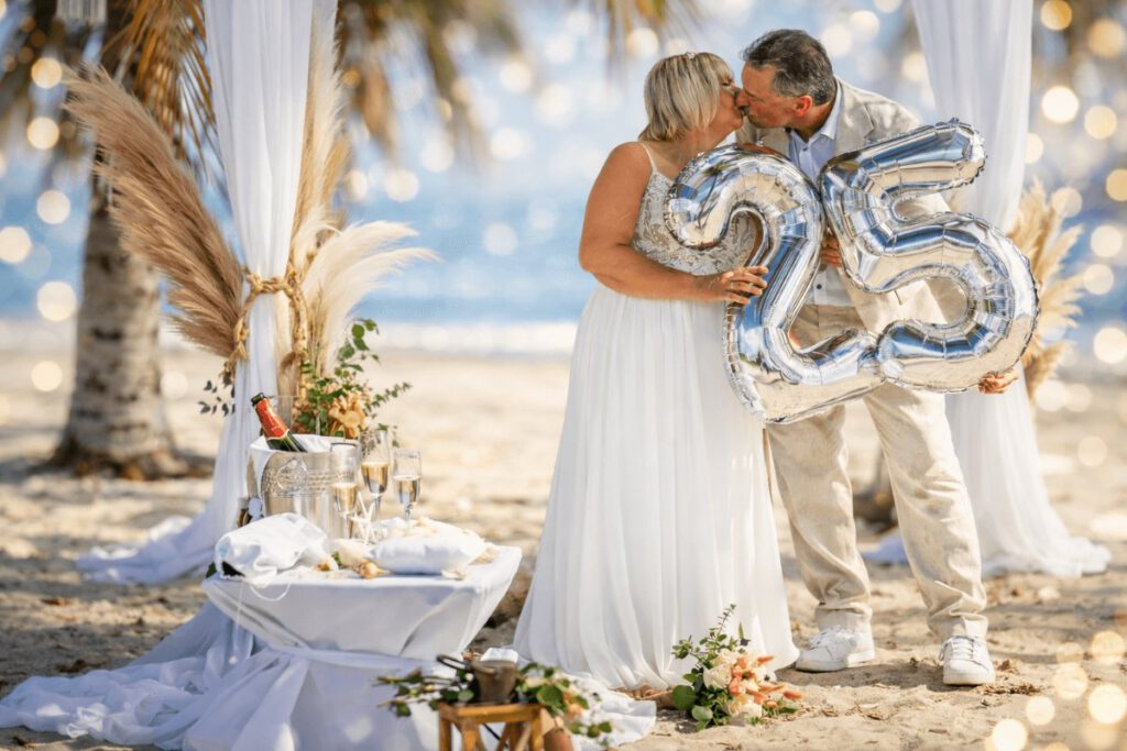 Silberpaar am Strand unter Palmen halten eine 25 in den Haenden Boho Deko